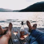 man and woman relaxing by lake drinking wine