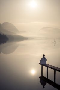 man meditating on lake dock