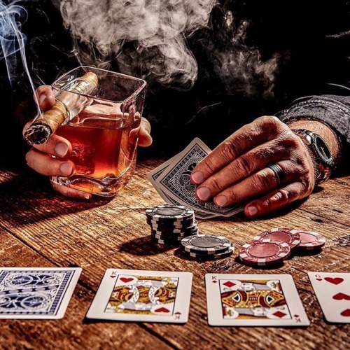 man playing poker drinking whickey and smoking a cigar