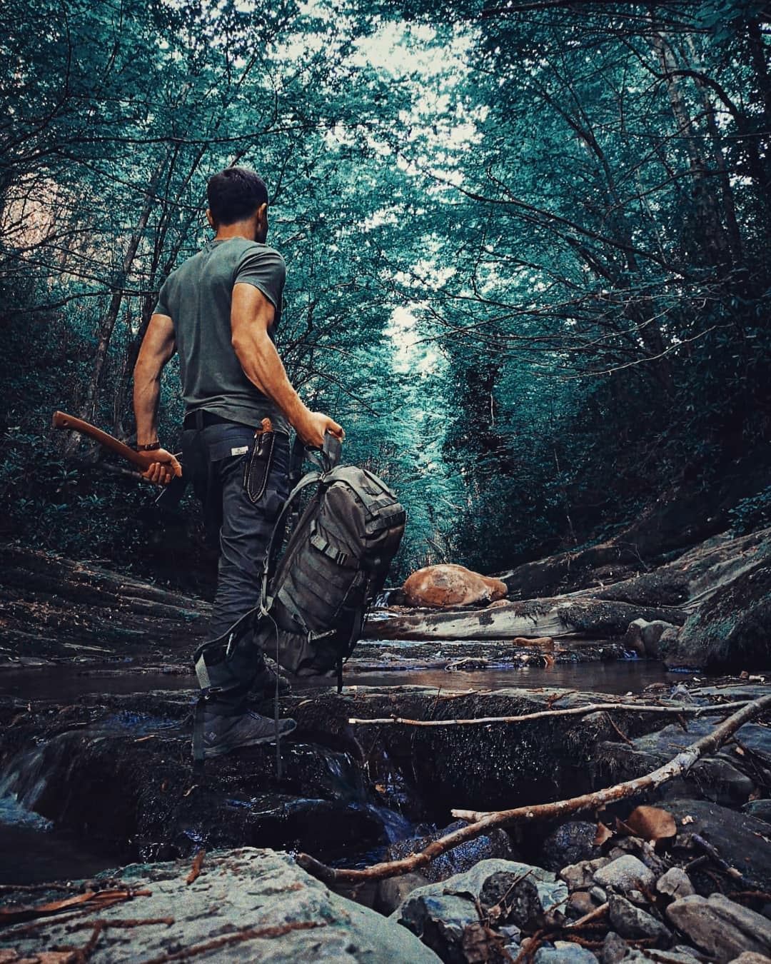 man walking through forest carrying survival gear